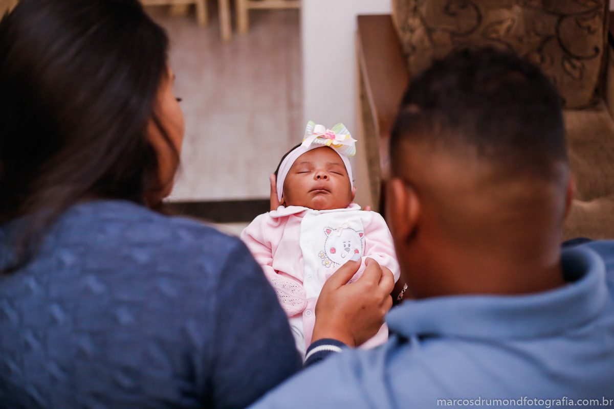 A fotografia da criança está em foco onde os pais estão segurando a mesma nos braços na sala da casa deles, eles estão sentados no sofá