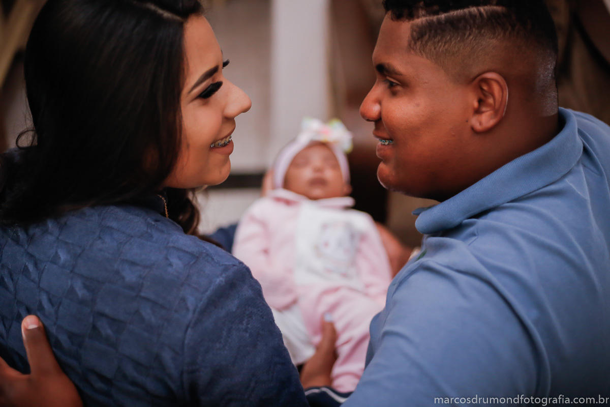 Fotografia de família na casa do cliente, os pais estão segurando a criança nos braços e a foto está desfocando a criança 