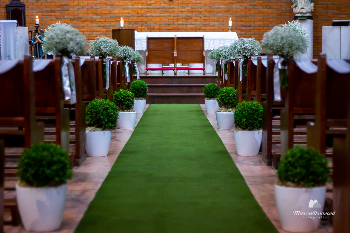 Fotografia colorida da igreja preparada para o casamento de Carole Varlei, tapete verde no piso, ornamentação perfeita e velas acesas para o início da cerimônia