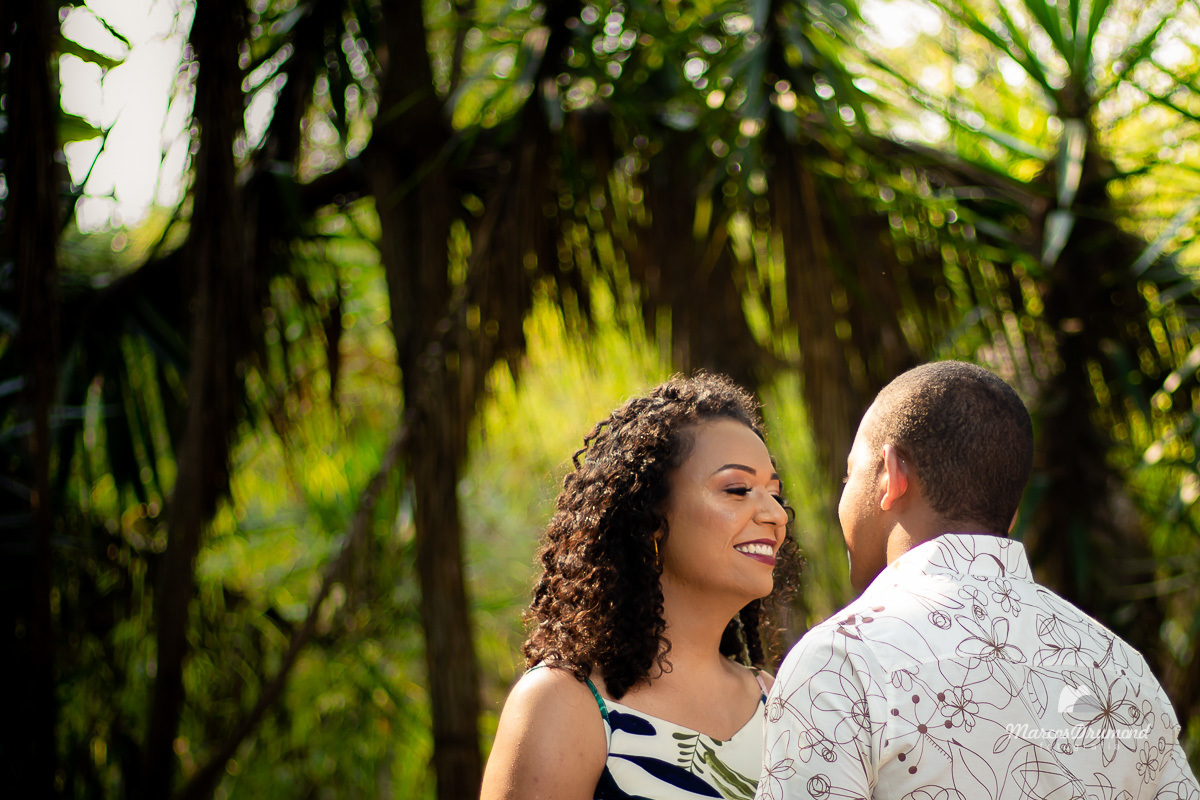 Linda fotografia colorida de pré casamento, onde os noivos estão de frente e sorrindo, a noiva está muito feliz e dando inúmeras gargalhadas onde há uma linda paisagem no fundo da foto