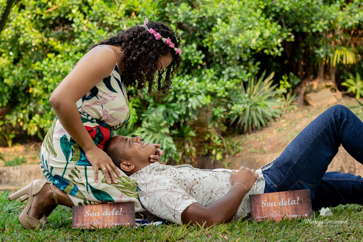 Fotografia de pré casamento onde o noivo está deitado no colo da noiva e ela está com uma mmão no rosto dele e a outra mão na perna dela ambos estão sendo fotografados em um sítio que houve a locação para as fotos do pré wedding