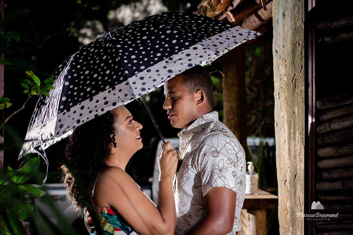 Fotografia de pré casamento com o casal usando uma sombrinha olhando um para o outro