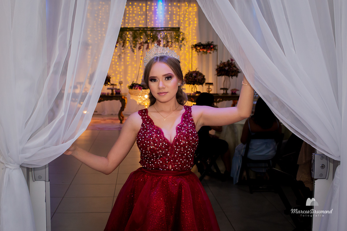 Aniversário de 15 anos da debutante Lívia Mascarenhas, onde ela está usando um vestido vermelho com um arco branco na cabeça e segurando nas laterais dos tecidos na entrada do salão de festas onde foi comemorado o seu aniversário de 15 anos, a debutante 