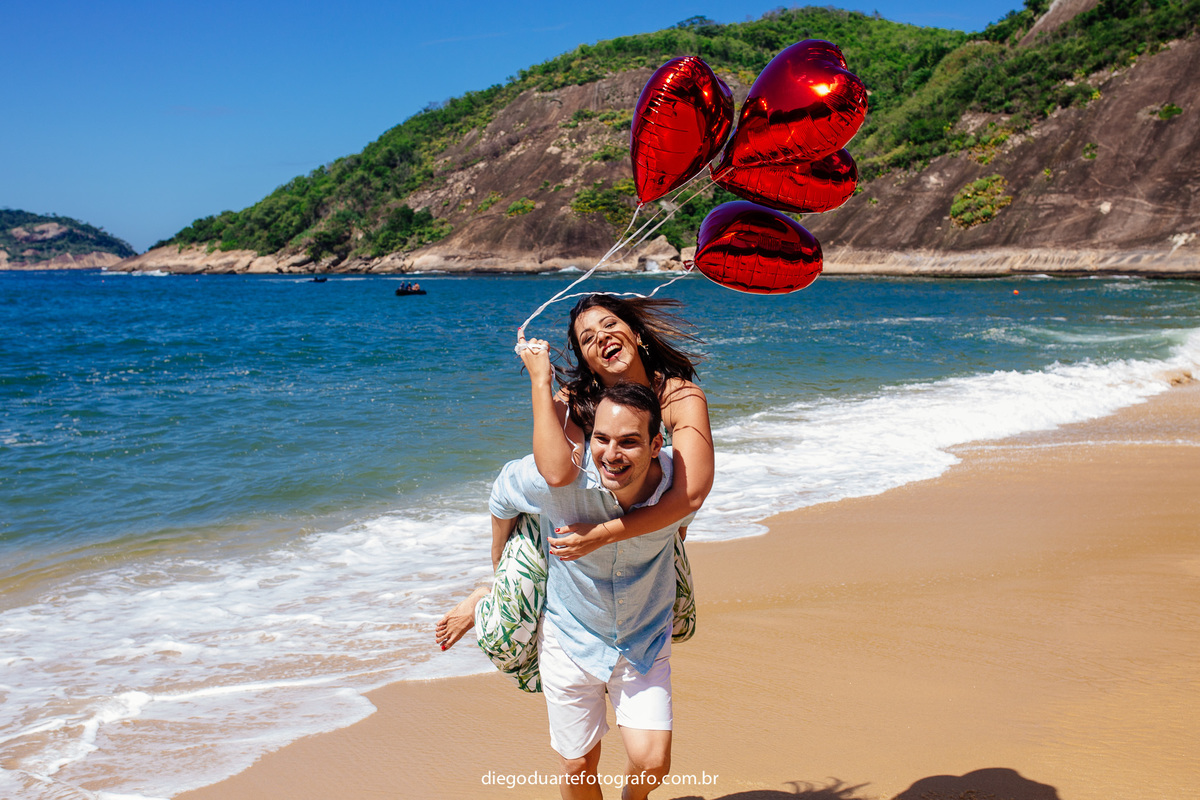 noivo carregando a noiva nas costas, praia vermelha, ensaio de casal, ensaio pre wedding, ensaio com balões de corações