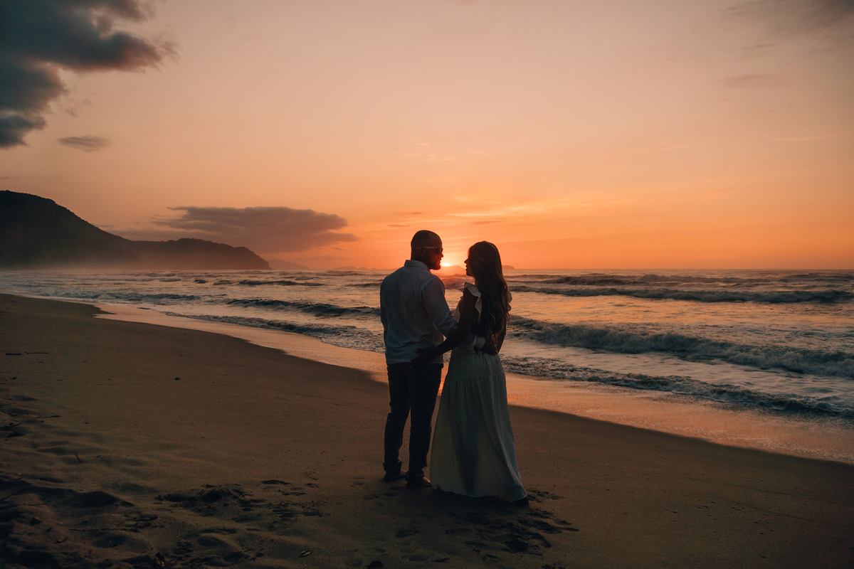 Casal contemplando o pôr do sol durante ensaio fotográfico na praia de Ubatuba.
