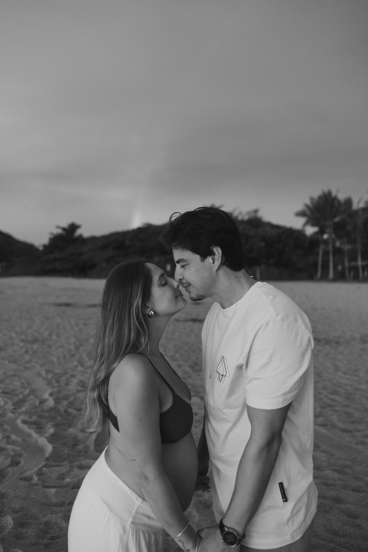 Casal celebrando a gestação durante ensaio ao ar livre no litoral.