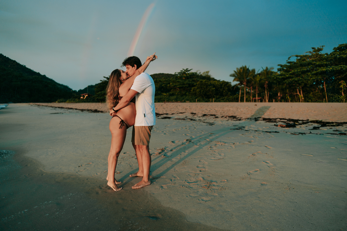Casal celebrando a gestação durante ensaio ao ar livre no litoral.
