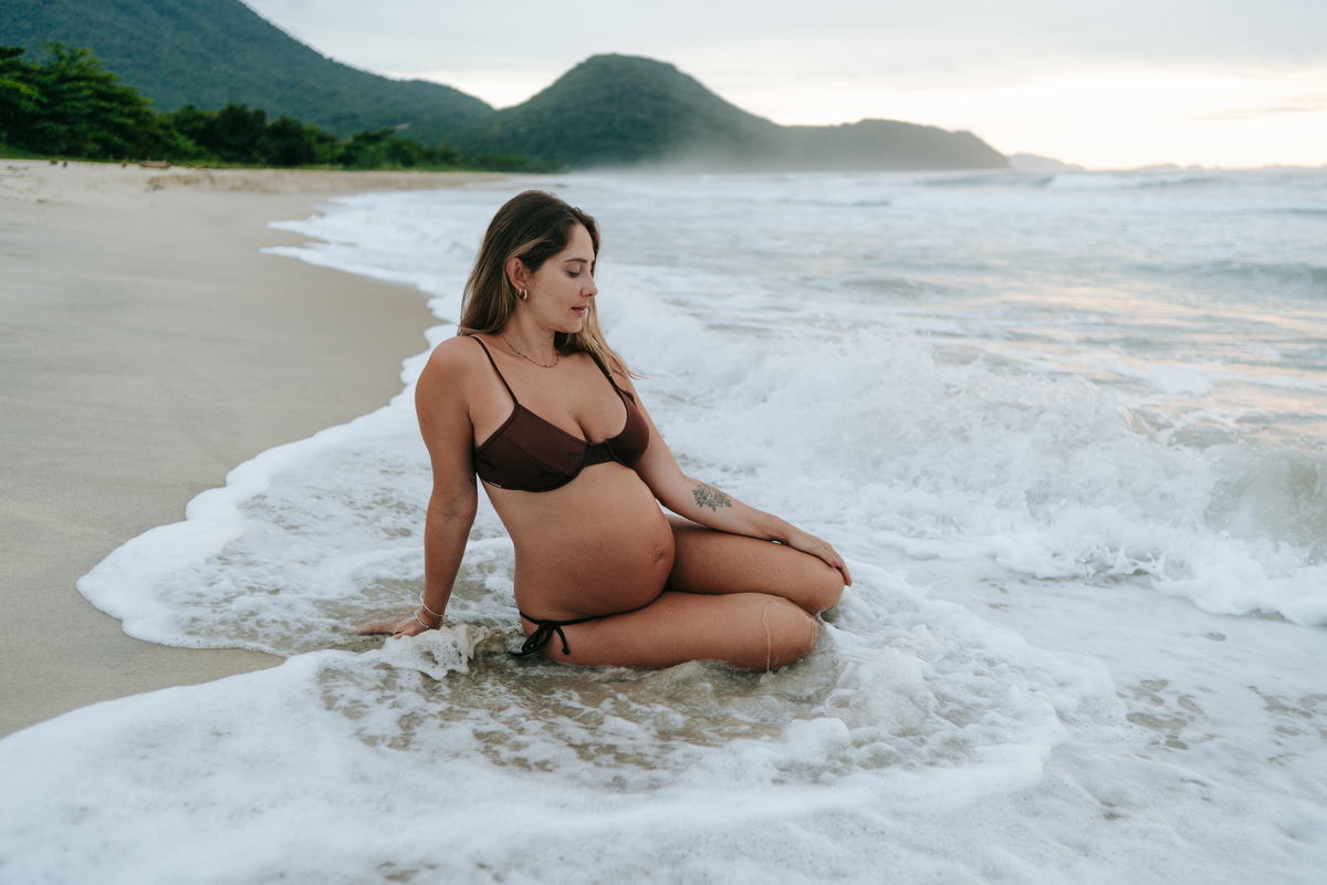 Mulher grávida aproveitando o mar durante ensaio de maternidade na praia.