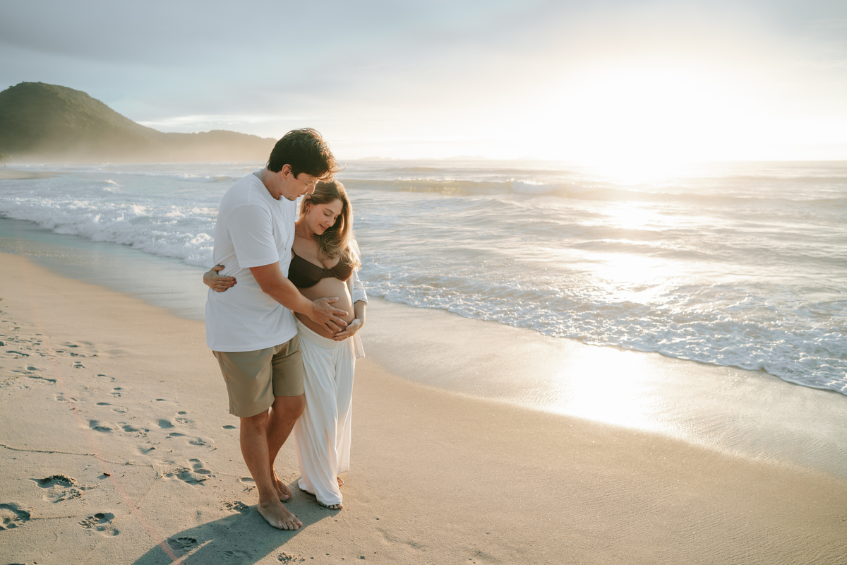 Futuros pais abraçados durante ensaio fotográfico ao nascer do sol.