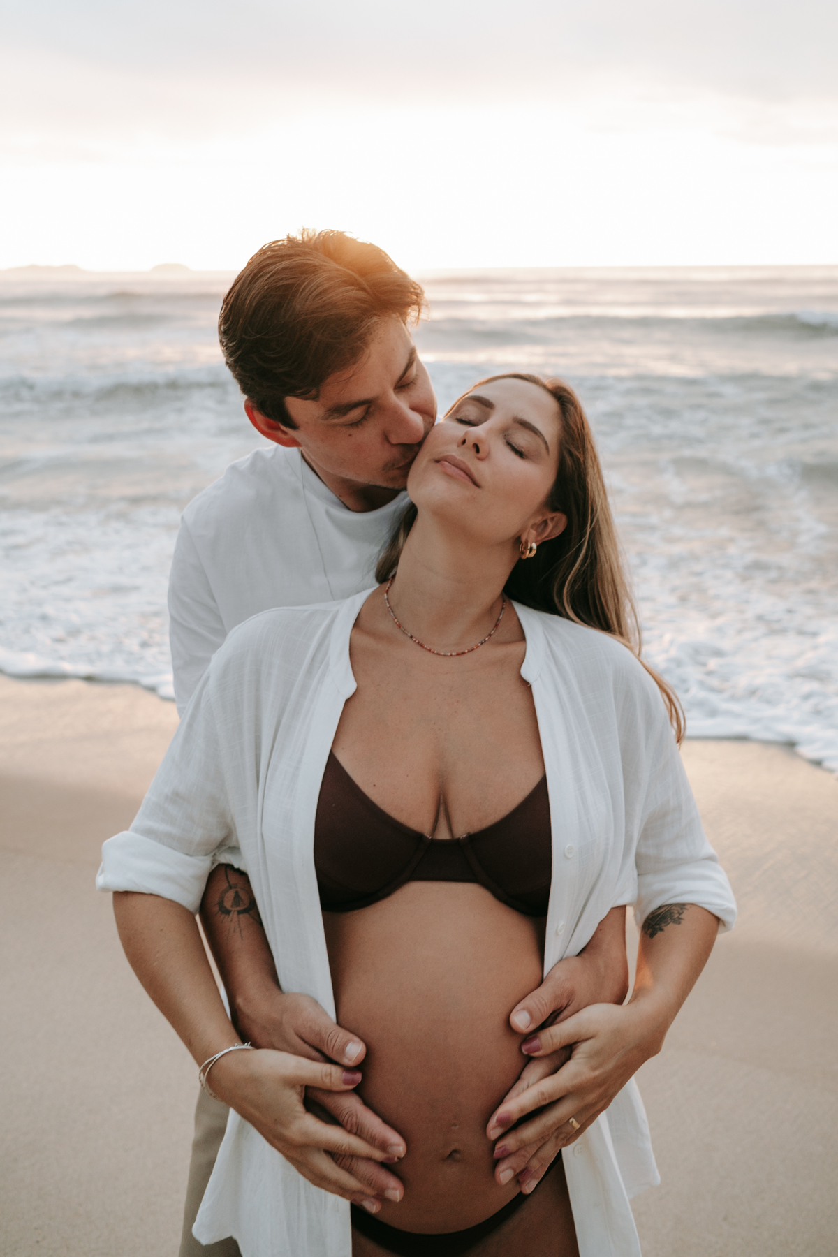Fotografia de casal esperando o bebê em cenário natural na praia.