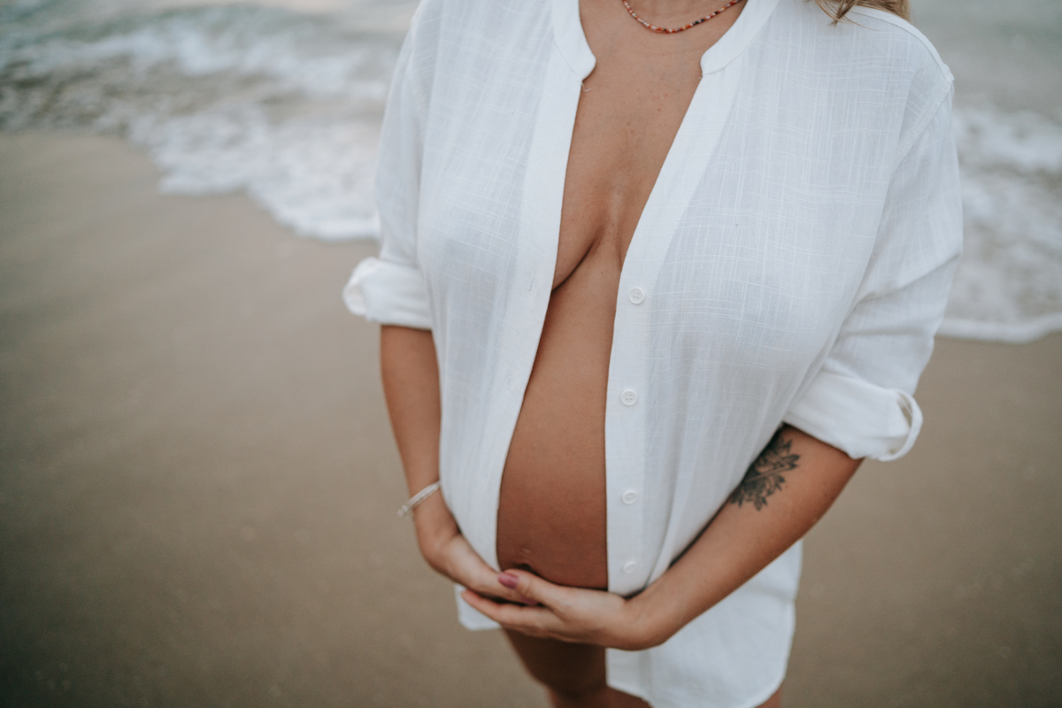 Fotografia de gestante em Ubatuba destacando a barriga durante ensaio na praia.