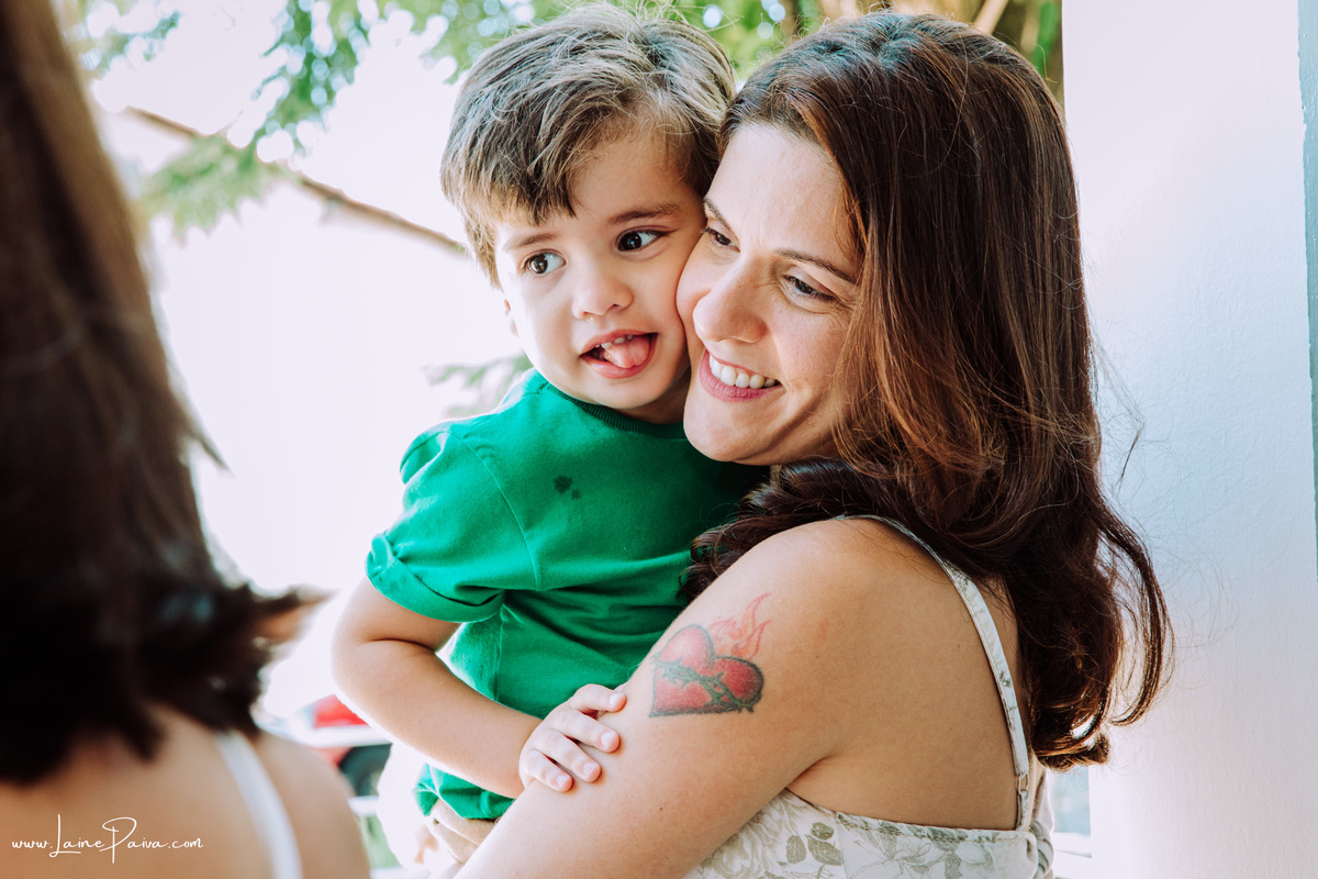 Criança no colo da mãe e com a lingua de fora em batizado de amiga