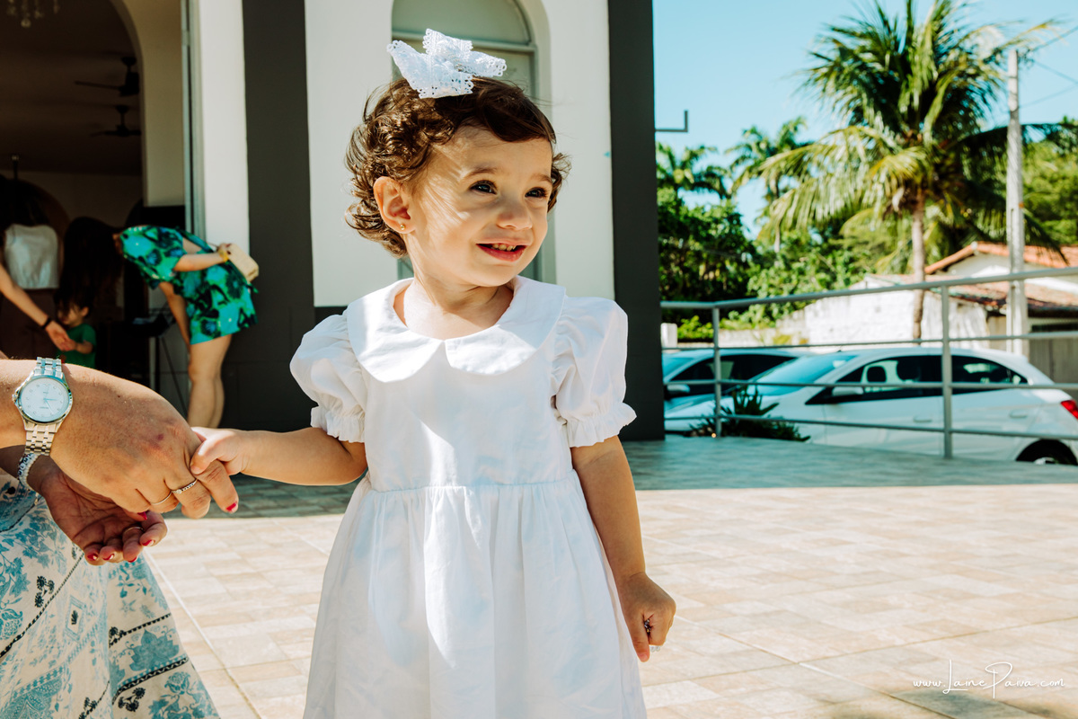 Criança sorrindo e olhando para o lado em seu batizado