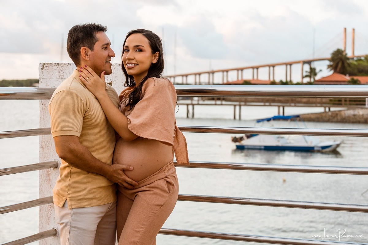 Dayza e seu companheiro celebram a espera pela primeira filha, Maria Laura, em um ensaio gestante no Complexo da Rampa, em Natal, com o pôr do sol sobre o Rio Potengi.