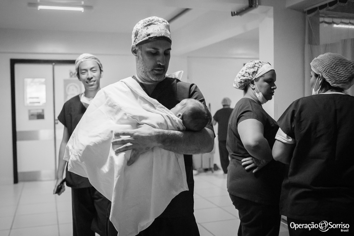 cirugião da OPeração Sorriso leva criança para os pais no colo