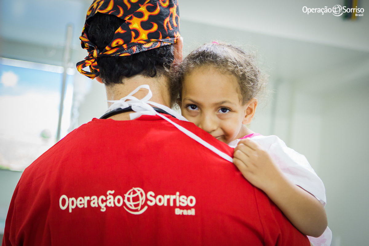 anestesista e voluntario da Operação Sorriso levando criança no colo e menina olhando e sorrindo