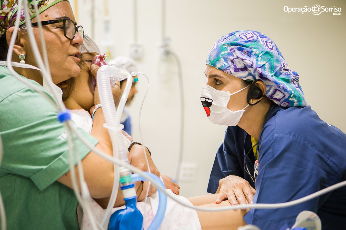 menina sendo abraçada pela anestesista e enfermeira