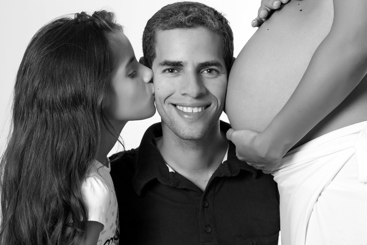 filha beijando pai e barriga de esposa colada no outro lado do rosto