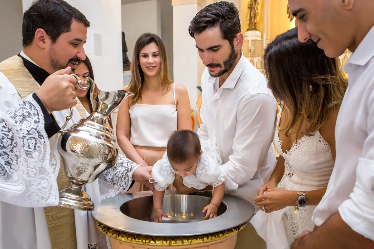 padrinho segura bebe enquanto padre se prepara para batizar criança