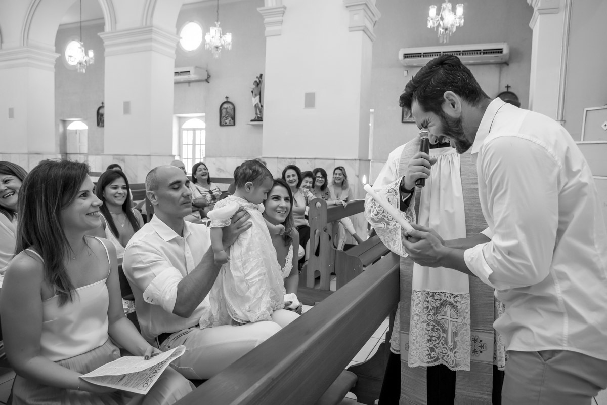 padrinho segura vela batismal e sorrir ao falar com afilhado