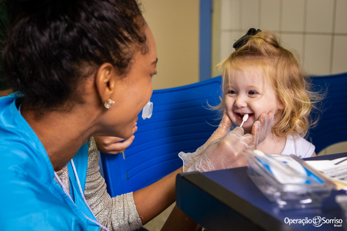 geneticista fazendo coleta de criança enquanto ela sorrir
