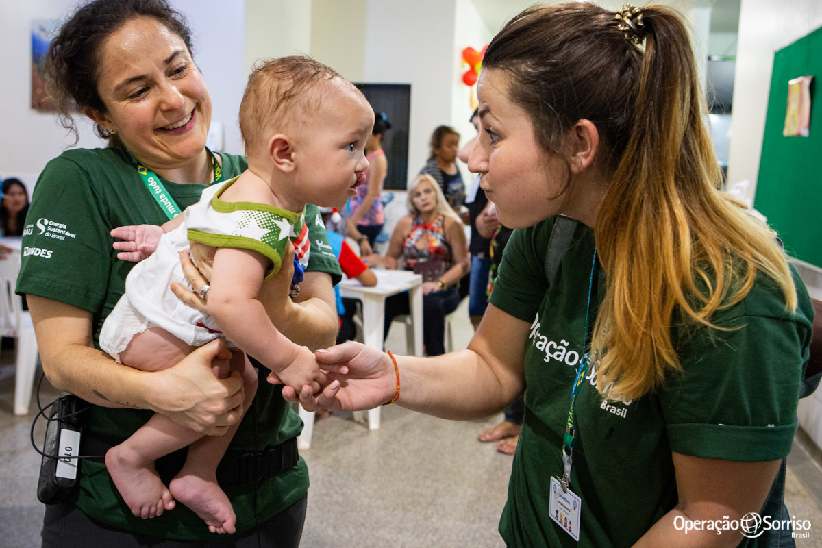 mulher brincando com bebe enquanto outra o segura