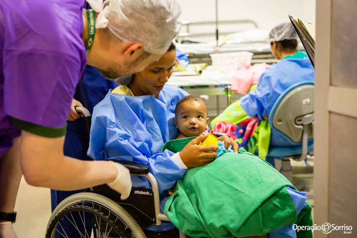 mãe abraçada com filho após a cirurgia e voluntário conversando com a criança

