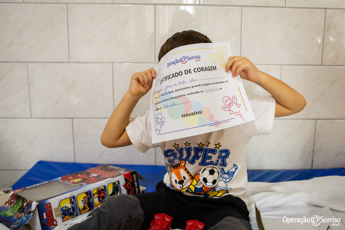 criança com certificado de coragem na mão cobrindo o rosto