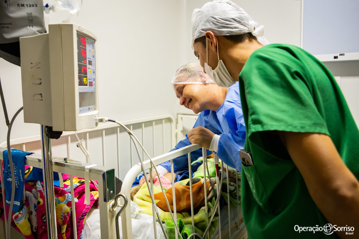 mãe e voluntário olhando criança após cirurgia