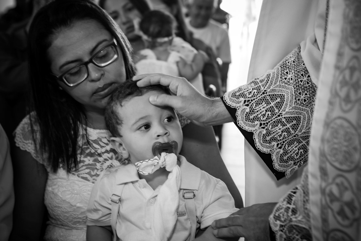 criança olhando para a o padre enquanto ele faz sinal da cruz em sua testa