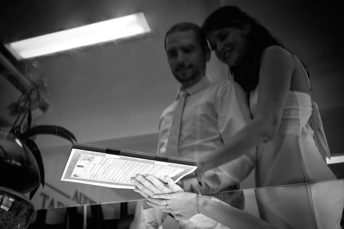 noivos com mão em cima da certidão de casamento e se olhando no reflexo da mesa em cartório de Parnamirim