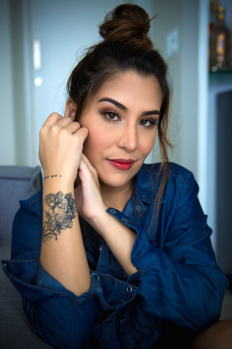 mulher sentada ao chão encostada no sofá com mão no rosto e camisa de botão jeans