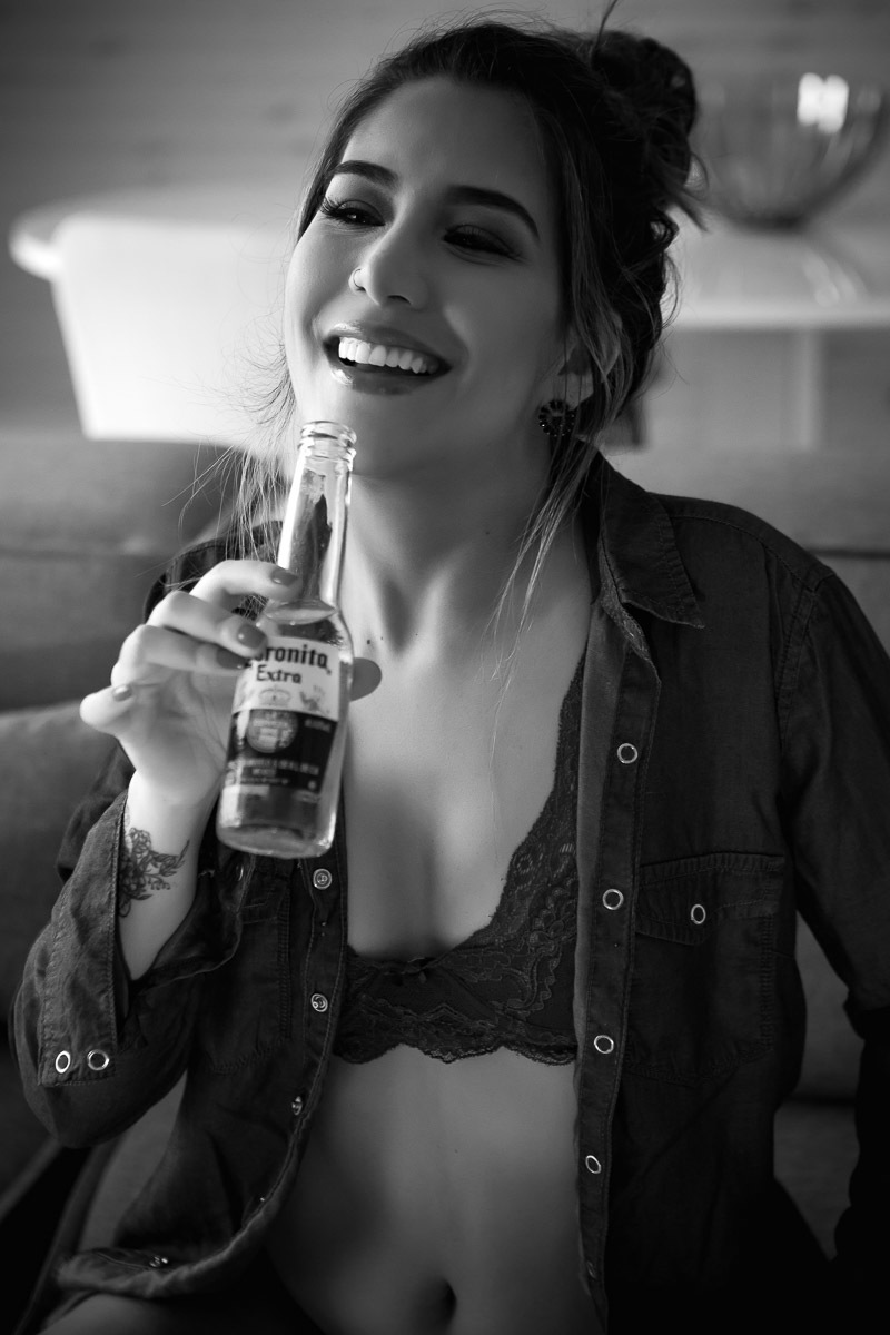 mulher sentada no sofá e tomando cerveja com camisa de botão jeans aberta