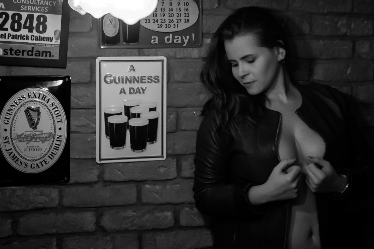 mulher encostada na parede com jaqueta aberta sem sutiã olhando para baixo