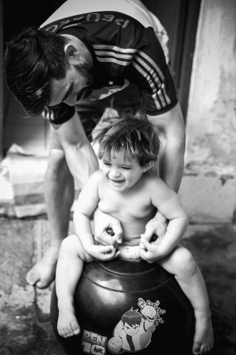 criança sentada em bola brincando e rindo com o pai