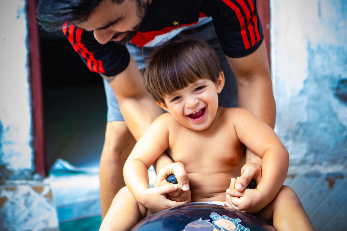 criança sentada em bola brincando e rindo com o pai