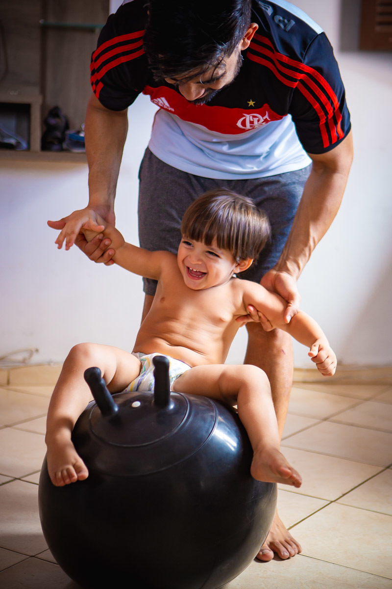 criança sentada em bola brincando e rindo com o pai que o segura