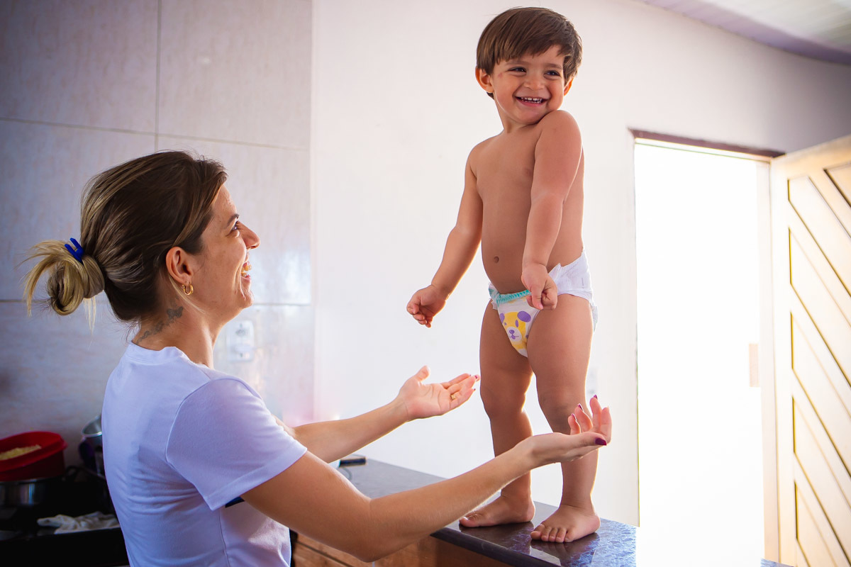criança em pé em balcão rindo com a mãe