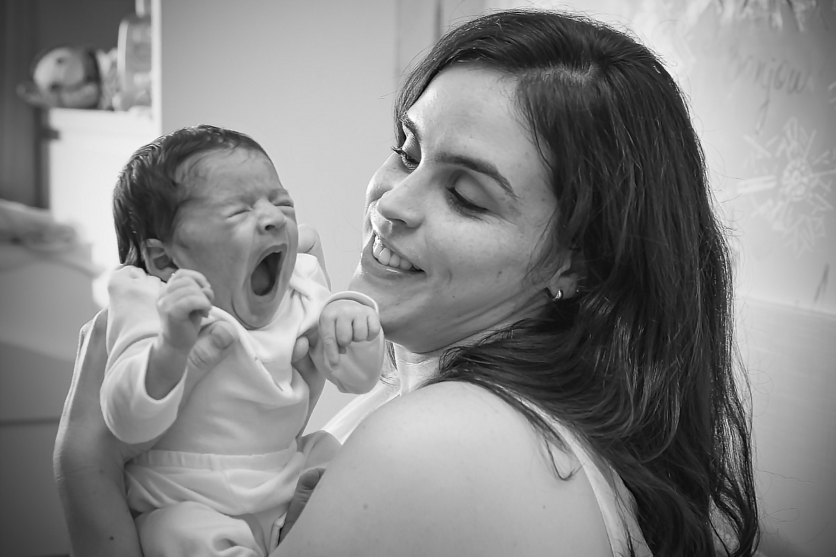 mãe segurando bebe no colo e olhando pra ela enquanto ela bocejar