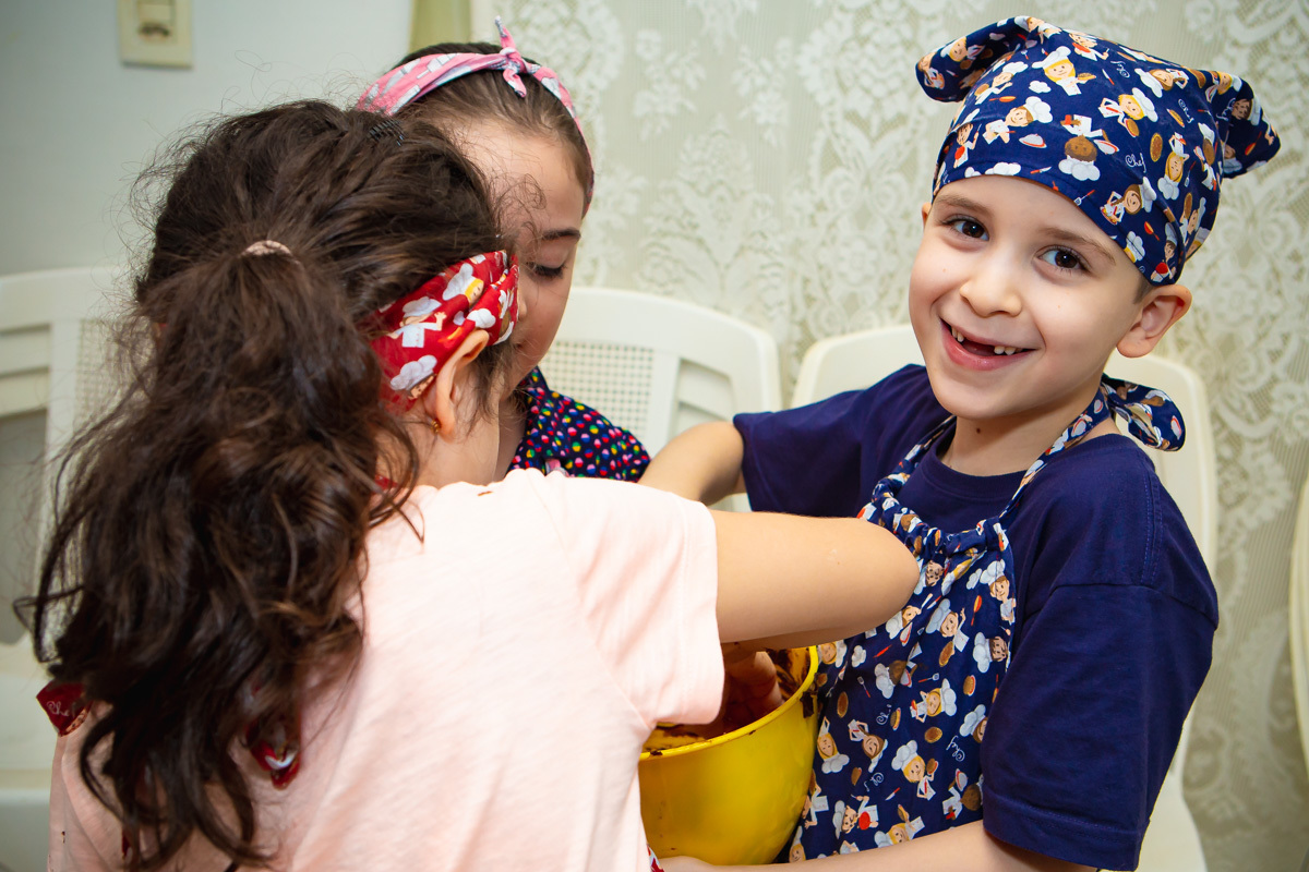 Crianças lambendo panela de massa de brownie. E menino olhando e rindo.