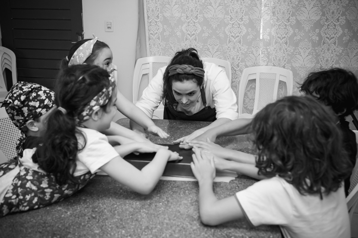 Crianças ajudando chef a bater no fundo da forma de bolo.