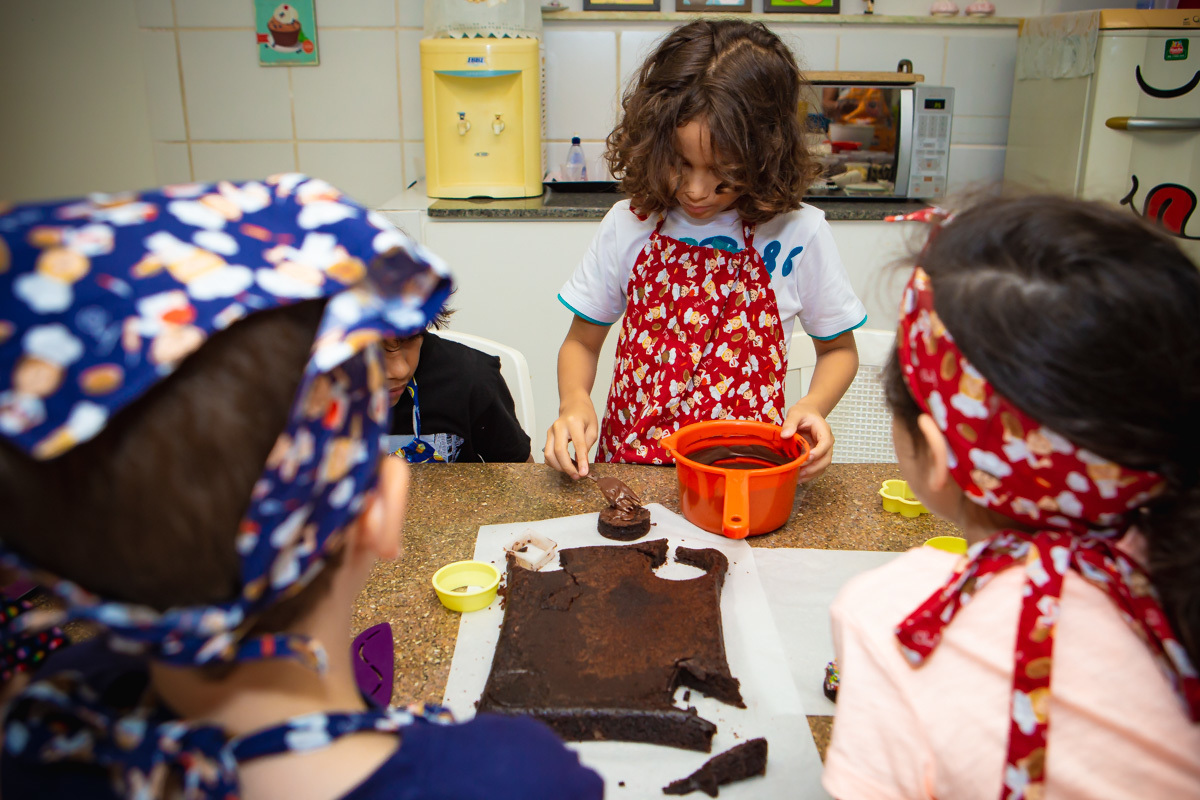 Criança decorando brownie e outras olhando.