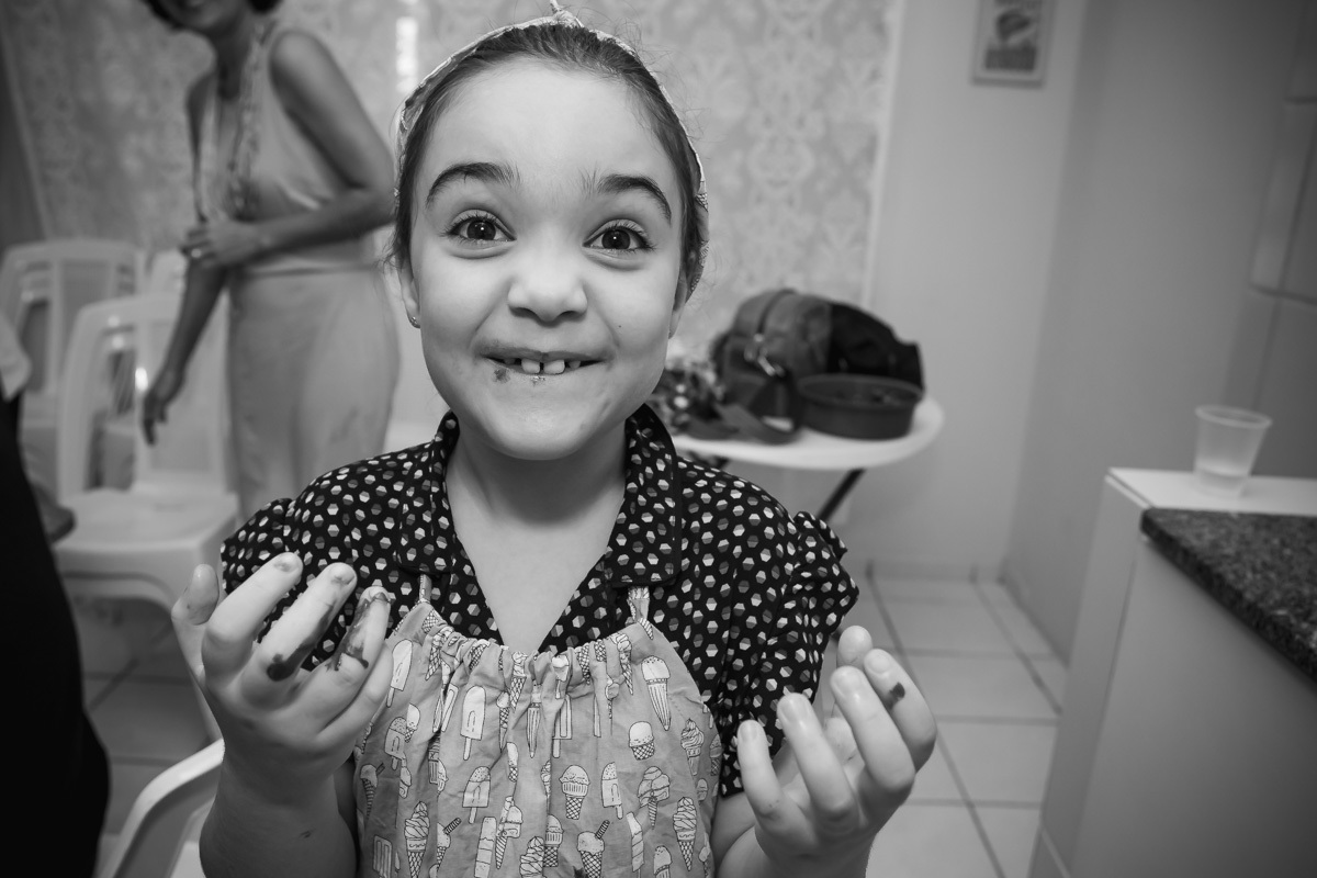 Menina com a boca e mãos sujas de chocolate olhando e sorrindo para câmera.