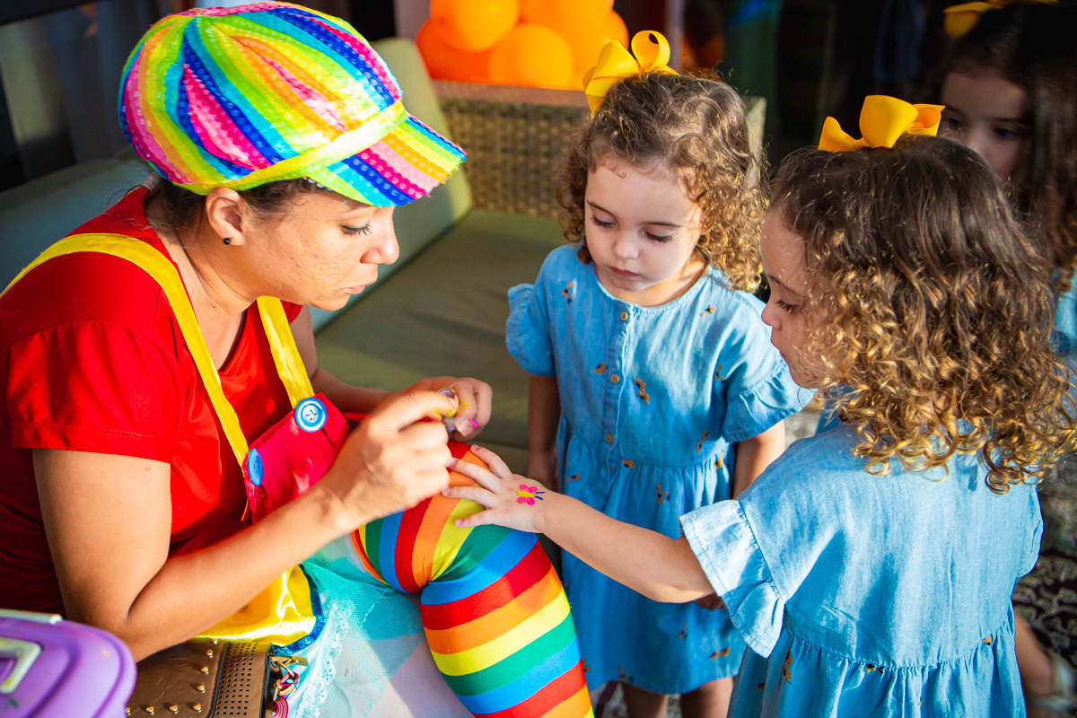Animadora desenhando borboleta na mão de criança enquanto sua irmã gemea olha