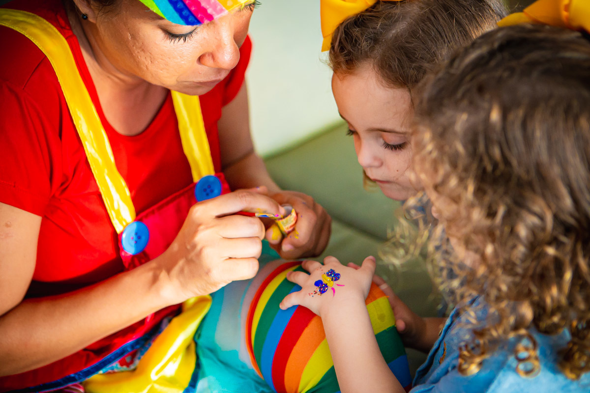 Animadora desenhando borboleta na mão de criança enquanto sua irmã gemea olha