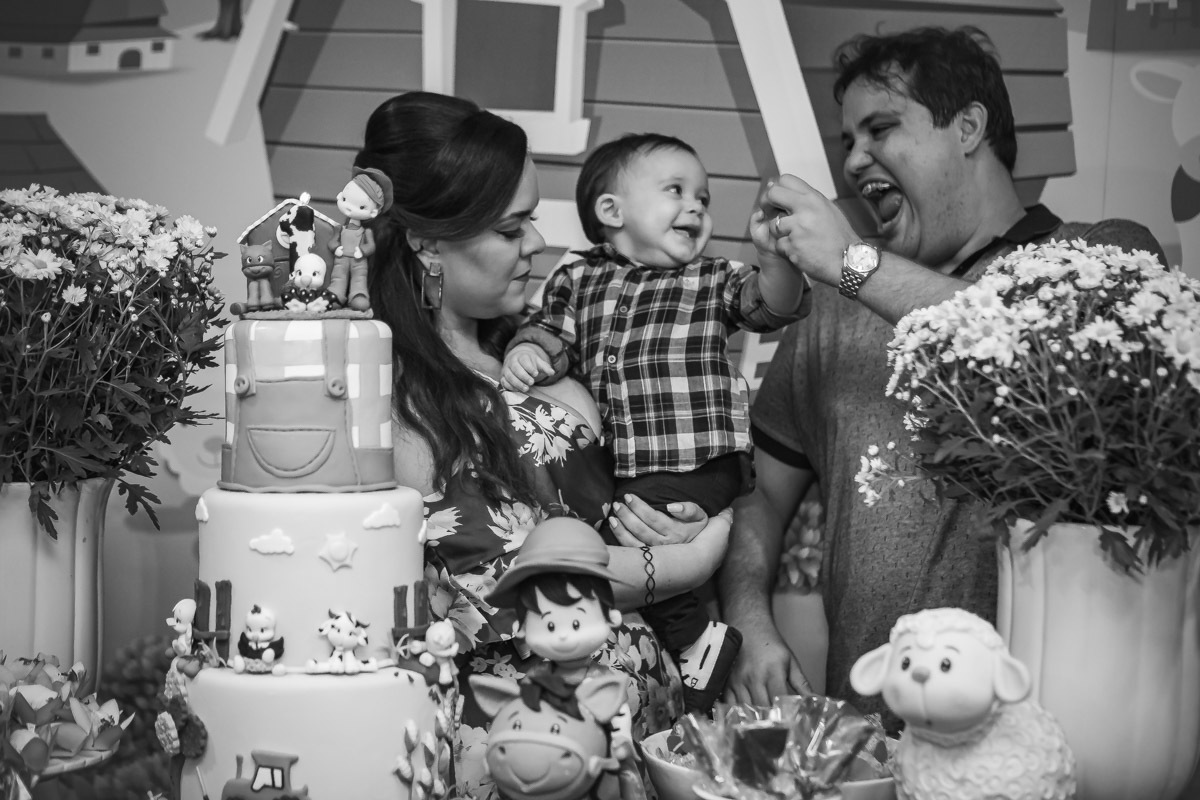 Pais olhando e animando aniversariante no colo em na hora do parabéns da festa com tema a fazendinha