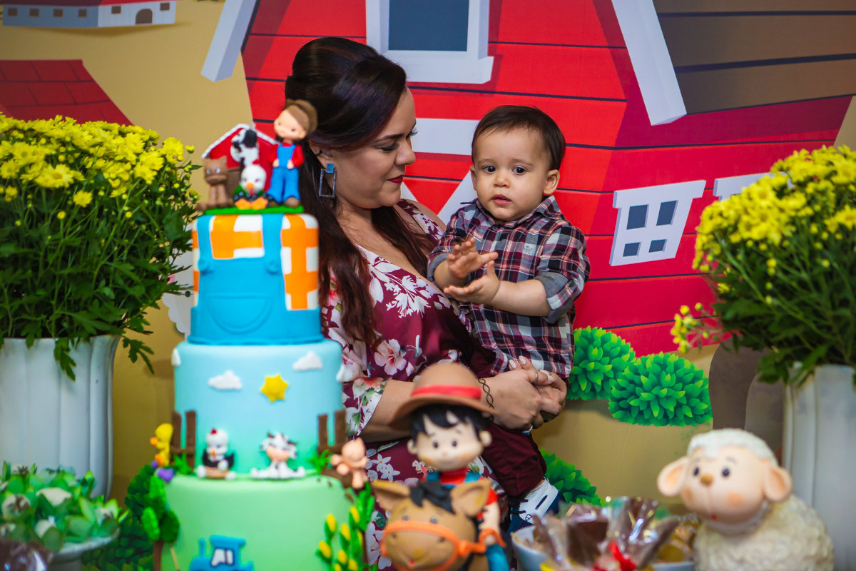 Mãe olhando para aniversariante no colo e cantando parabéns da festa com tema a fazendinha