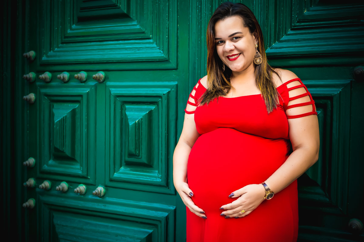 Gestante com mãos na barriga e encostada na porta verde da igreja São Francisco no pelourinho em salvador.