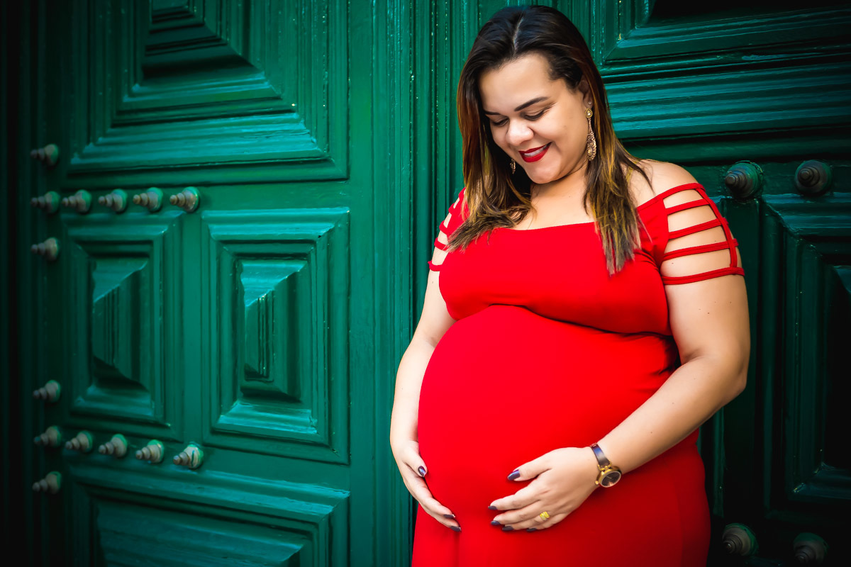 Gestante com mãos na barriga, olhando para ela e encostada na porta verde da igreja São Francisco no pelourinho em salvador.