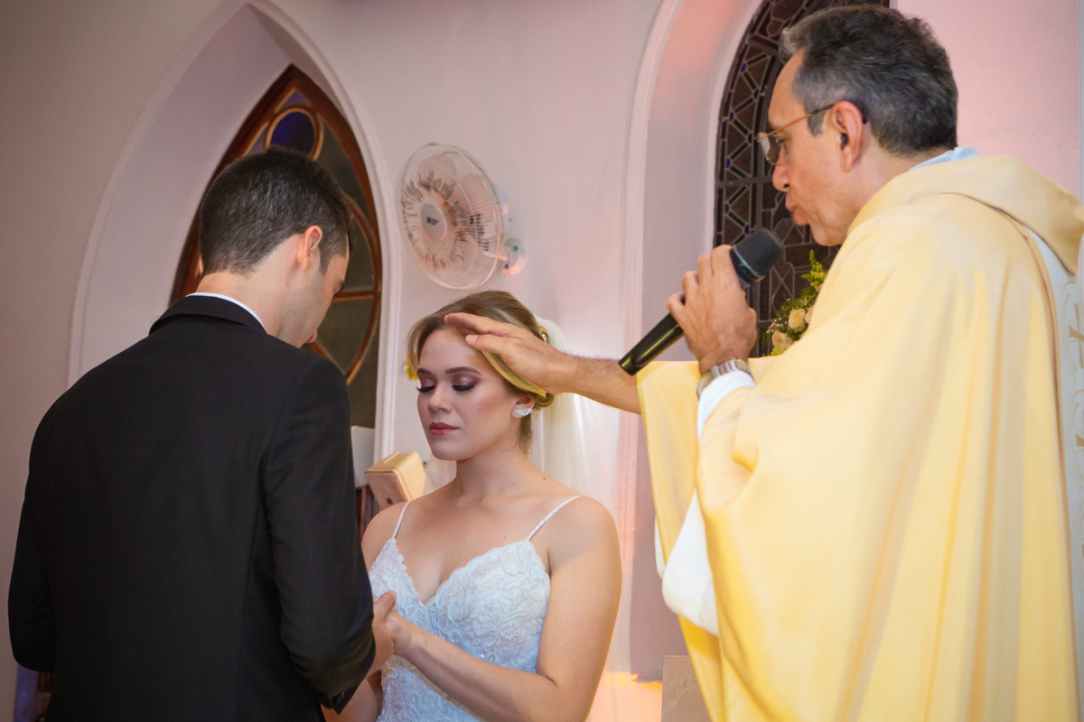 Celebração do casamento na Igreja Santa Terezinha, noivos de frente segurando e padre abençoando alianças